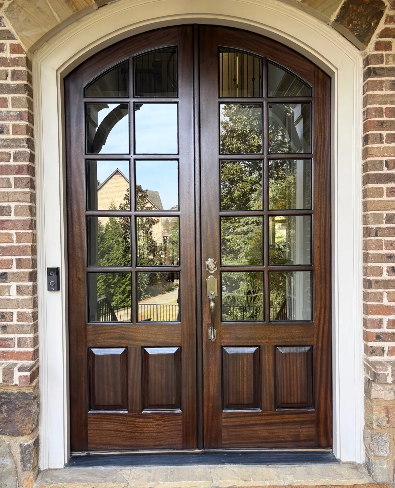 Arched wood double entry doors installed on a brick home
